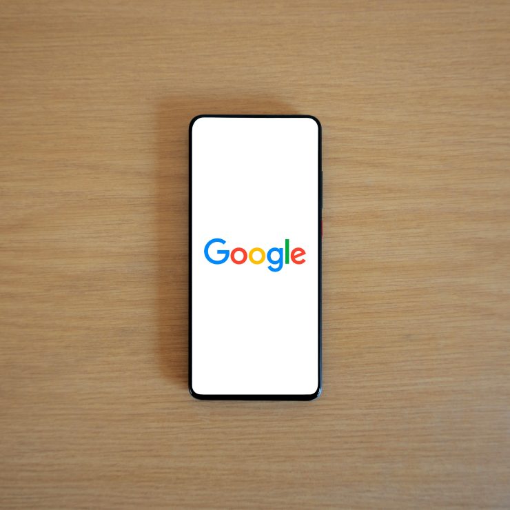 A smartphone displaying the Google homepage on a wooden surface, viewed from above.